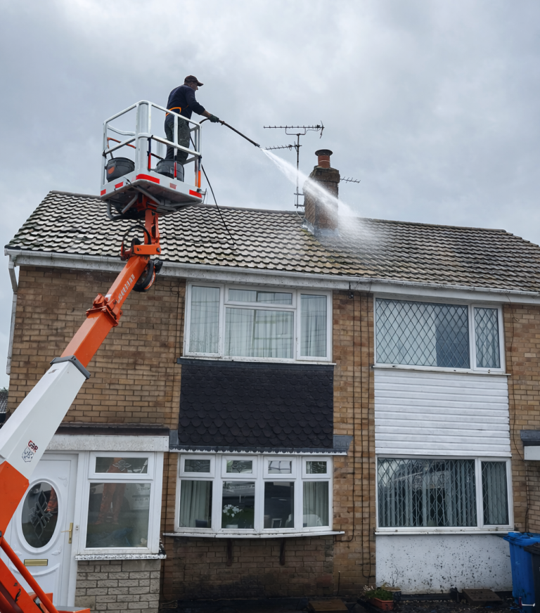 A person on a platform uses a pressure washer to clean a roof.
