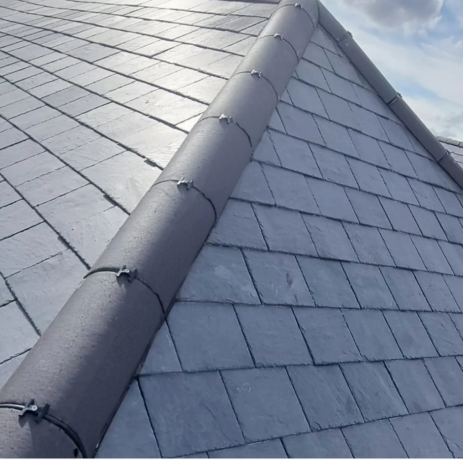 Close-up of a slate roof with a ridge and silver tiles under a bright sky.