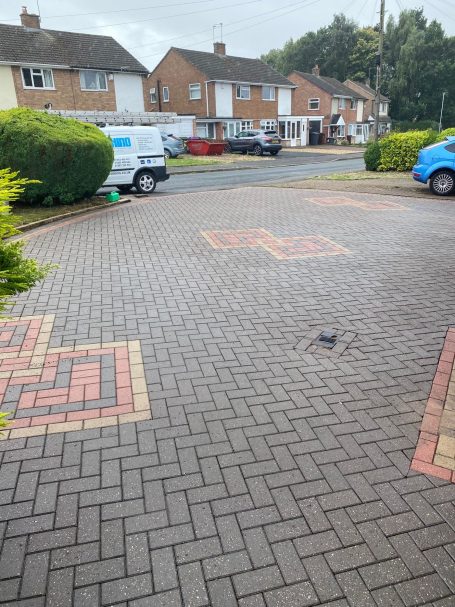 Paved driveway with patterned bricks and residential houses in the background.