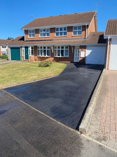 A brick house with a tarmac driveway and well-maintained front garden.