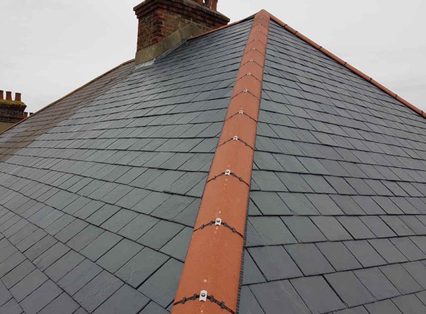 Slate roof with an orange ridge, showcasing a cloudy sky in the background.