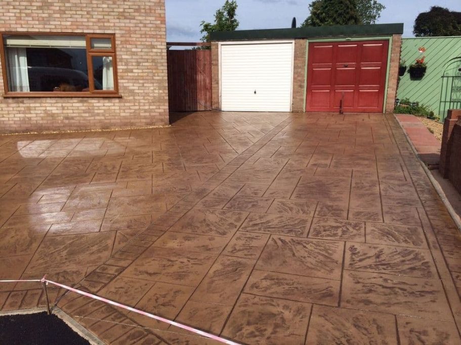Patterned concrete driveway in front of a house with a garage and garden.