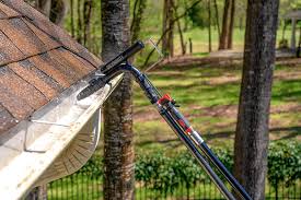 Gutter cleaning tool positioned on the edge of a roof amidst trees and grass.