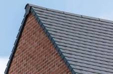 Close-up of a sloped roof featuring grey tiles and a brick wall.