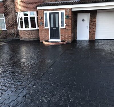 Black stamped concrete driveway with a brick house and two doors.